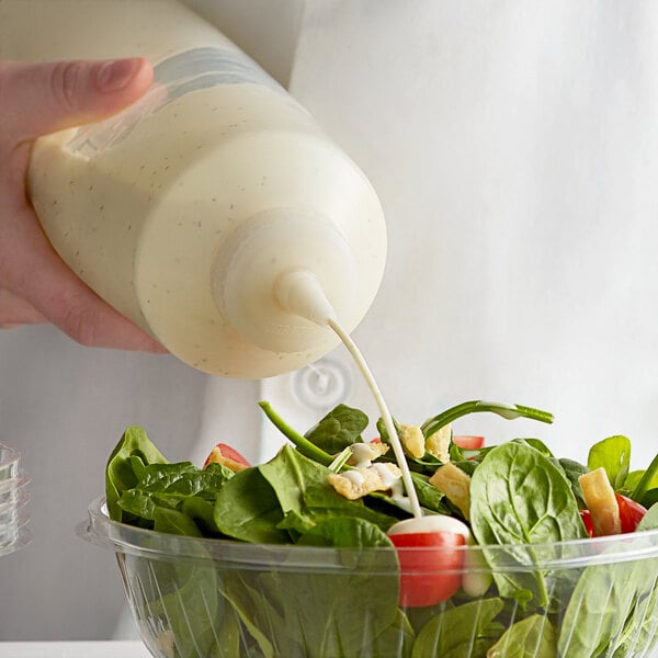 A person using a Vollrath clear squeeze bottle to pour dressing onto a salad.