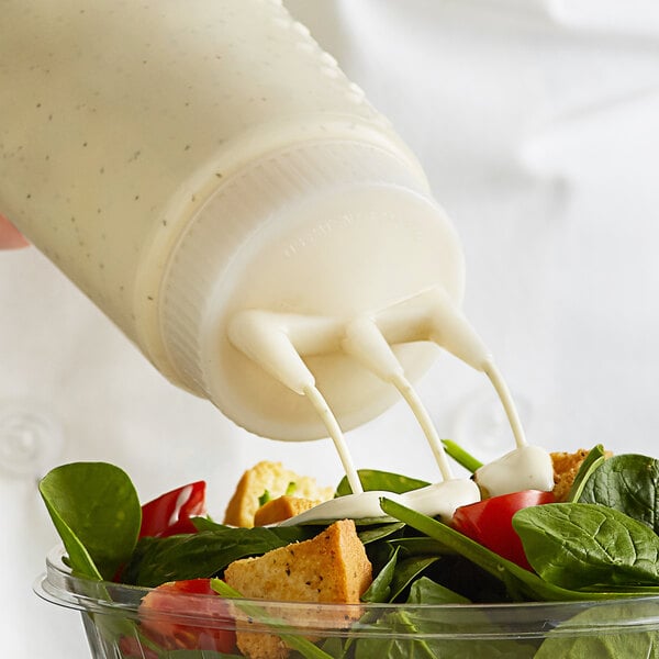 a person pouring mayo on a salad