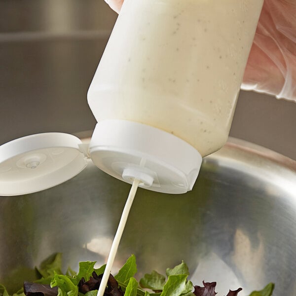 A hand using a white Vollrath squeeze bottle to pour dressing onto a salad.