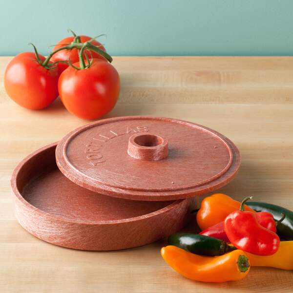 A red round HS Inc. polyethylene tortilla server with a lid on a table with tomatoes.