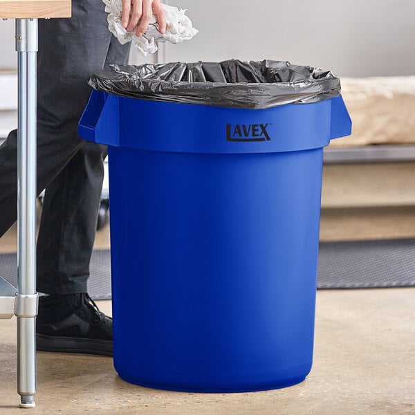 A man holding a Lavex blue plastic 32 gallon trash can.