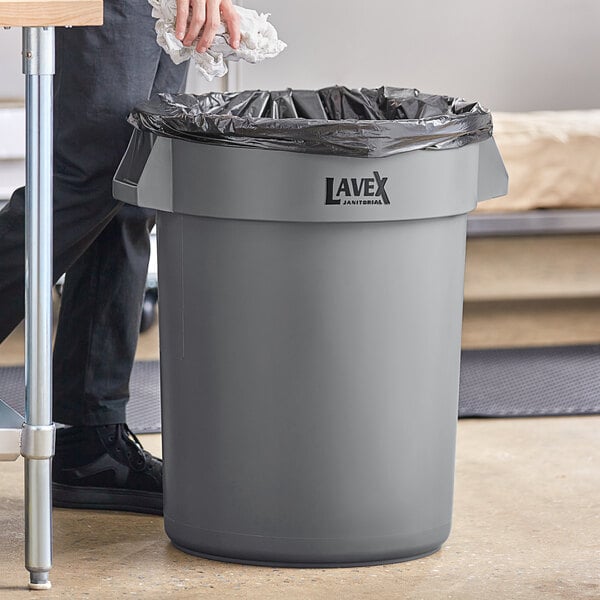 Person throwing waste out into a 32 gallon gray trash can