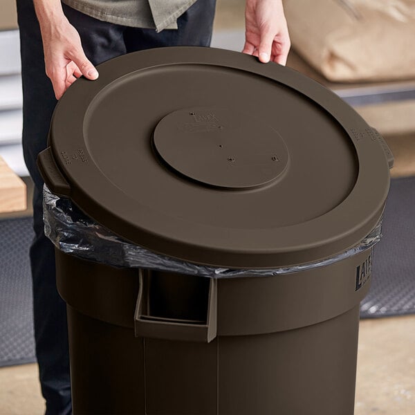 A person holding a brown Lavex round commercial trash can lid.