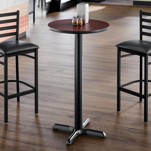 A round bar height table with a reversible cherry and black top and a cast iron base.