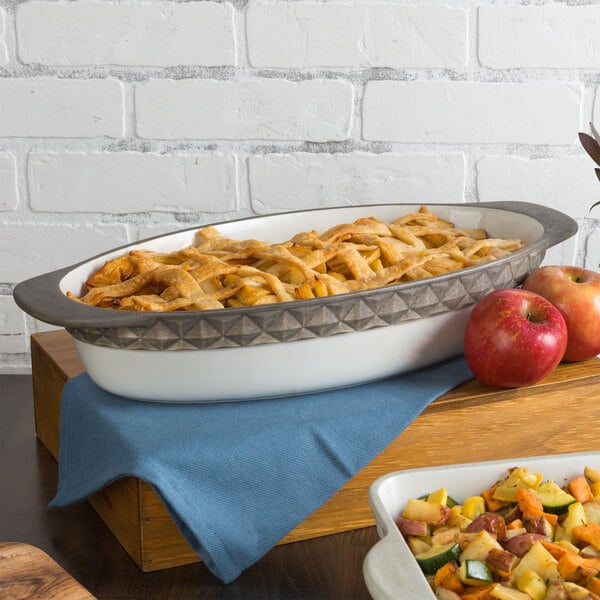 A Tuxton black truffle band oval casserole dish filled with apples and vegetables on a table.