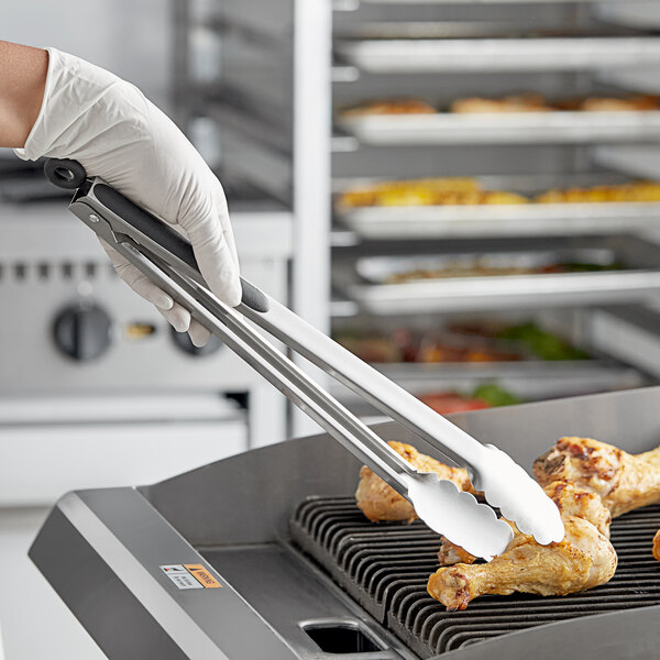 A person in gloves using Tablecraft locking tongs to pick up a chicken leg from a grill.