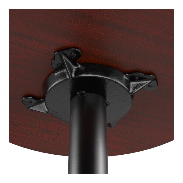 A close-up view of the underside of a round bar-height table with a cherry finish and a black cast iron base.