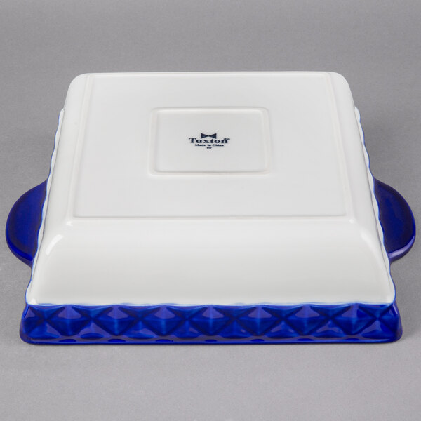 A white square Tuxton casserole dish with a cobalt blue band.