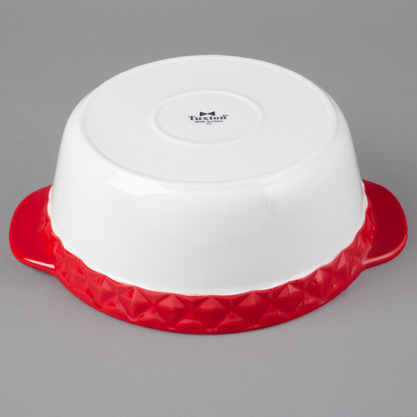 A white Tuxton round china casserole dish with red band and handles.