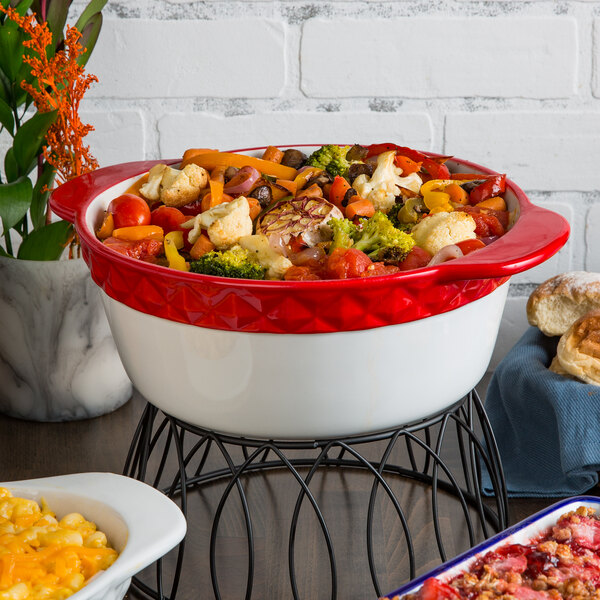 A Tuxton round red and white casserole dish filled with food on a table.