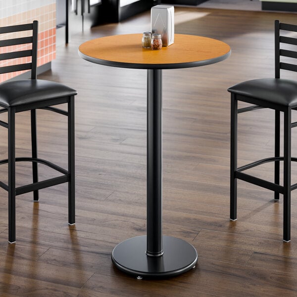 A round bar height table with a reversible walnut and oak top and a black cast iron base.