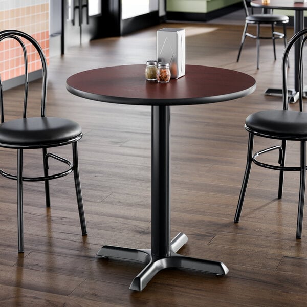 A round standard height table with a reversible cherry and black top and a cast iron base, set in a dining area.