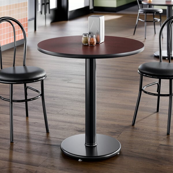 A round standard height table with a reversible cherry and black top and a 17-inch cast iron base, shown in a restaurant setting.