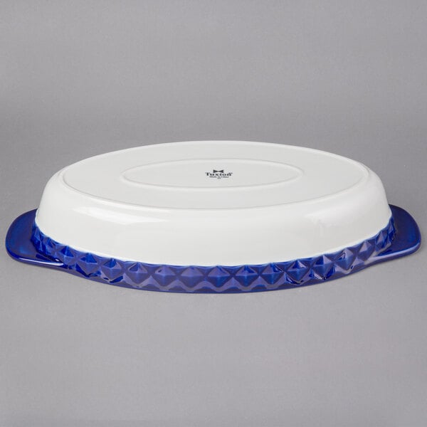 A white oval Tuxton casserole dish with a blue stripe.