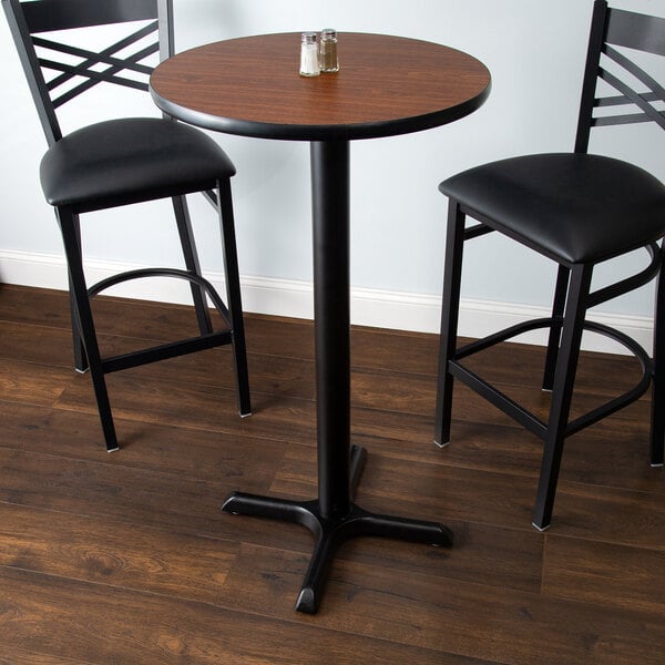 A Lancaster Table & Seating bar height table with a reversible walnut and oak top and a cross base plate with two black chairs.