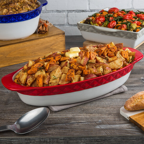 A Tuxton cayenne band oval casserole dish filled with food on a table.