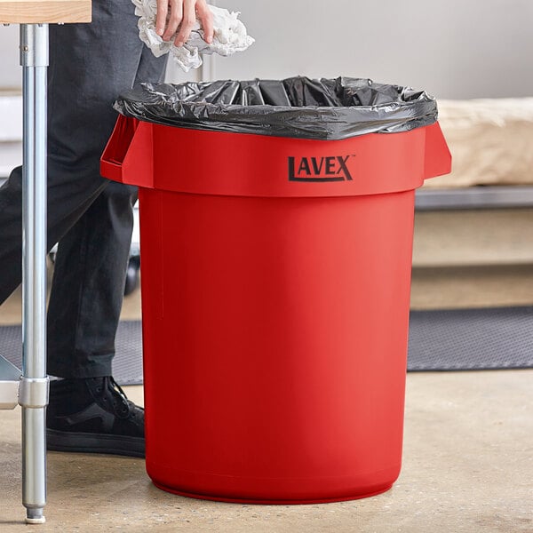 A man putting white paper in a Lavex red plastic utility trash can.