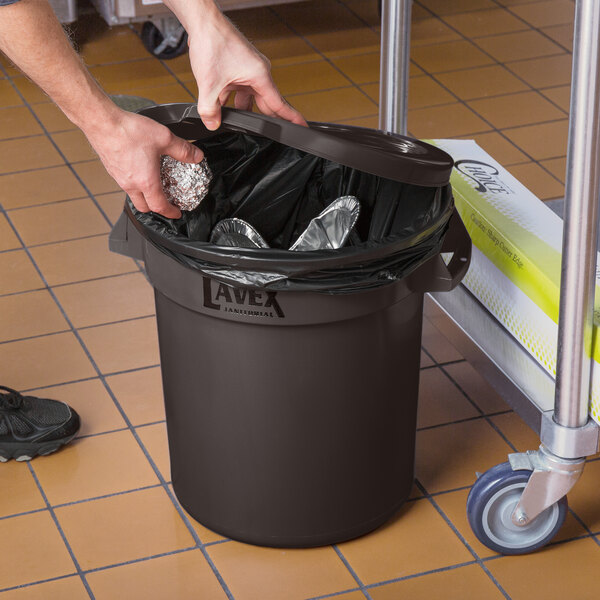 A person putting foil in a Lavex brown round trash can with a lid.