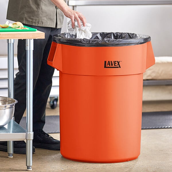 A man standing next to a Lavex orange high visibility commercial trash can.