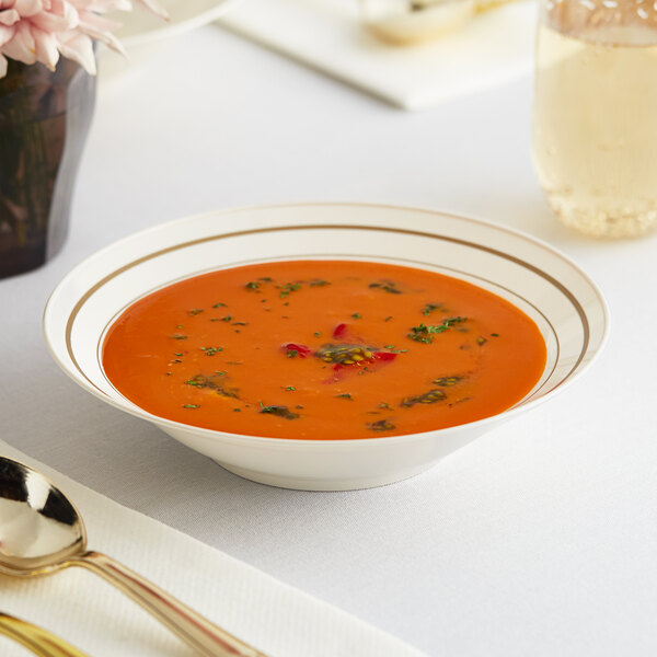 A WNA Comet ivory plastic bowl with gold accent bands filled with soup on a table.