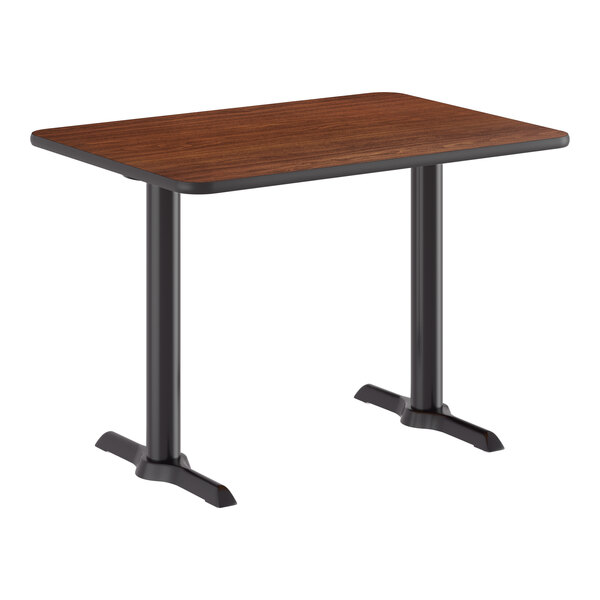 A rectangular standard height table with a reversible walnut and oak top and a black cast iron double pedestal base.