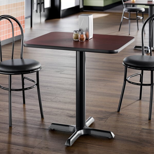 A square standard height restaurant table with a reversible cherry and black top and a black cast iron base.