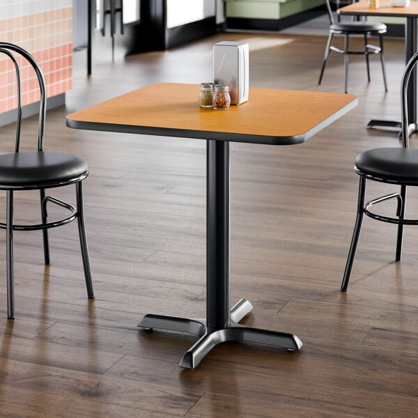 A square restaurant table with a reversible walnut and oak top and a black cast iron base.