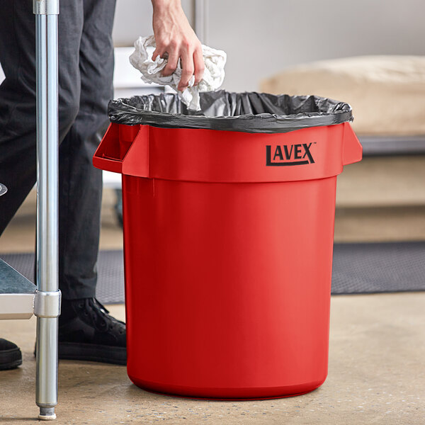 A man putting a trash bag in a red Lavex 20 gallon trash can.