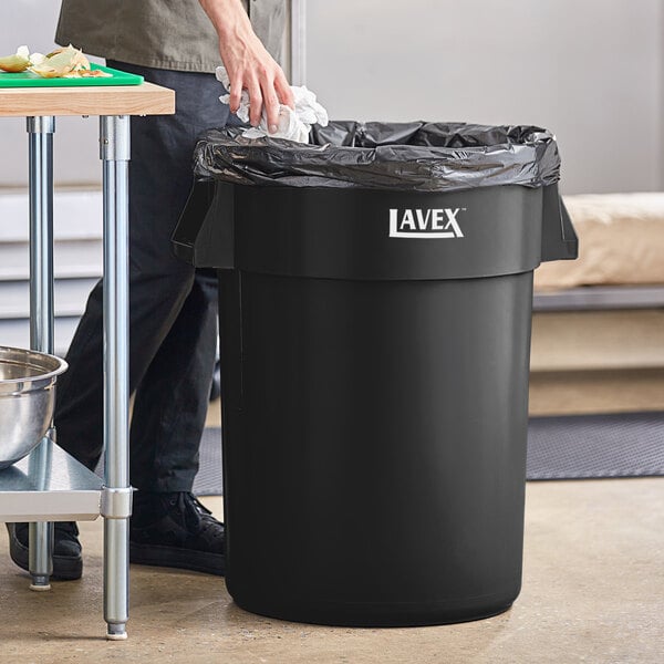 A man standing next to a Lavex black commercial trash can.