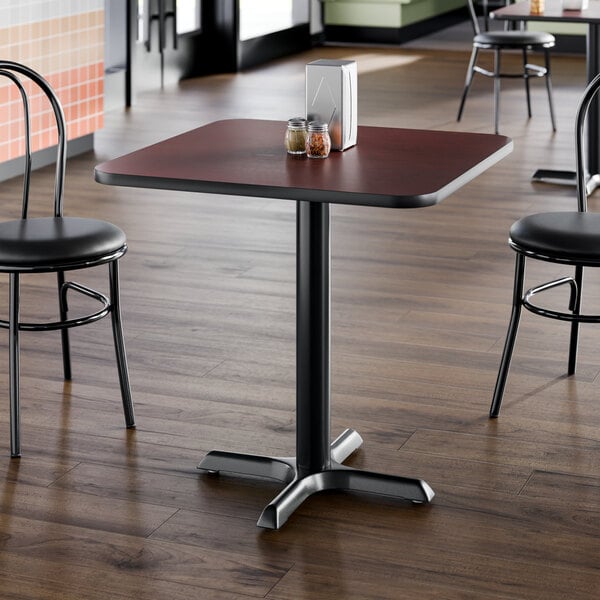 A square restaurant table with a reversible cherry and black top, supported by a black cast iron base.