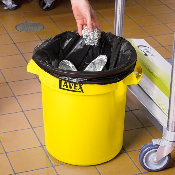 A person holding a yellow Lavex trash can lid over foil.