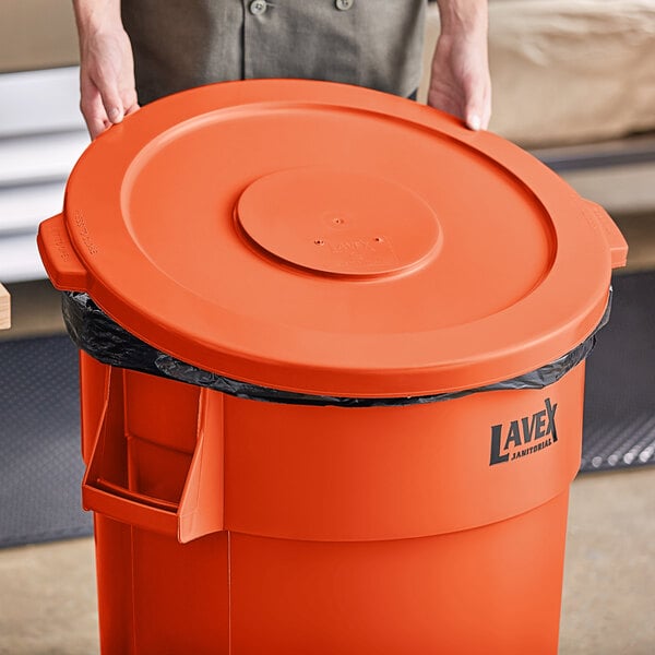 A person holding a large orange trash can lid.