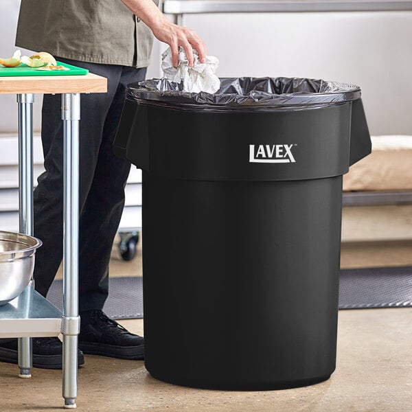 A man standing next to a Lavex black round trash can.