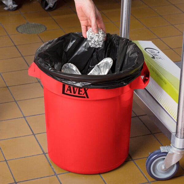 A person putting foil in a red Lavex trash can.