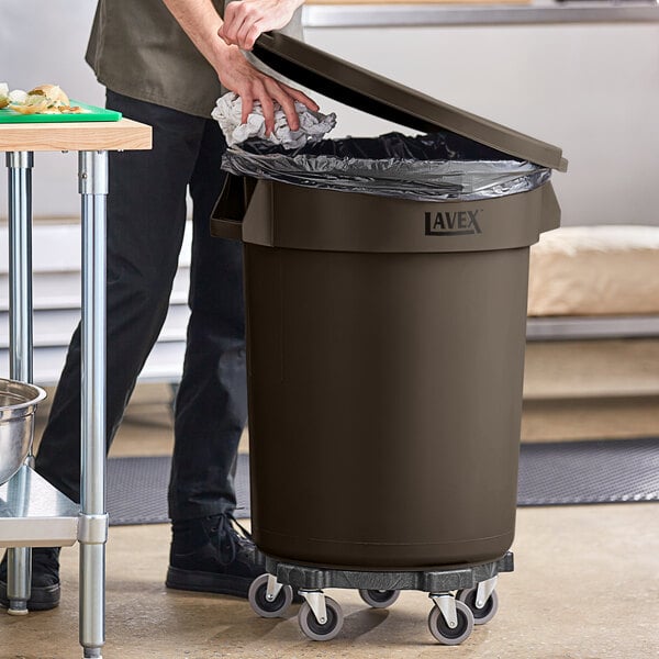 A man opening a Lavex brown round commercial trash can in a professional kitchen.