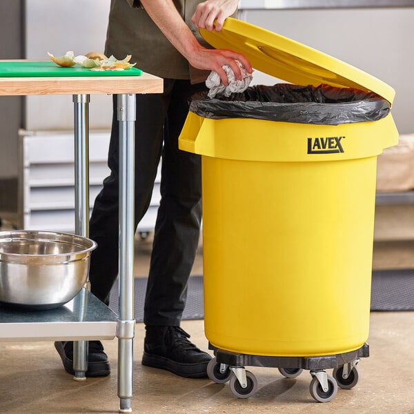 A man opening a yellow Lavex commercial trash can.