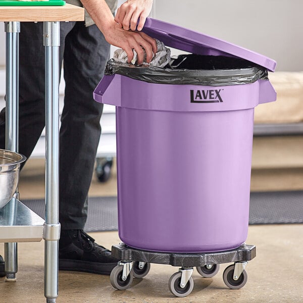 A person putting trash in a Lavex purple round commercial trash can.