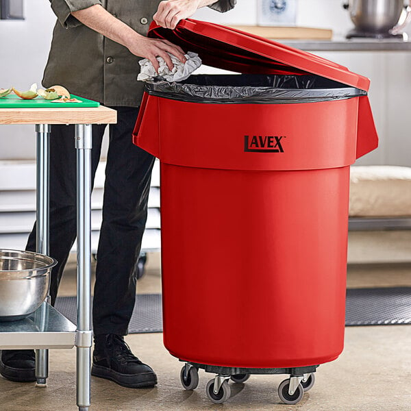 A woman standing next to a red Lavex trash can with a black lid.