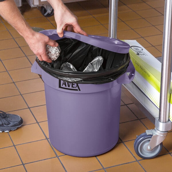 A person holding a Lavex purple round commercial trash can