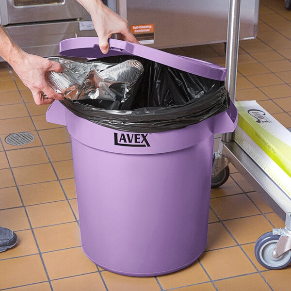 A person putting a bag in a Lavex purple trash can.