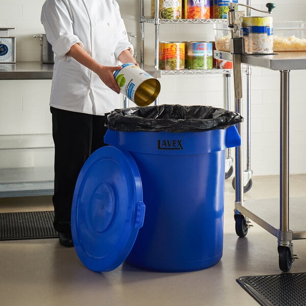 A chef pouring food into a Lavex blue trash can.