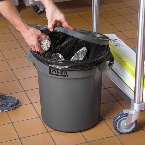 A person in a hospital cafeteria putting foil in a Lavex 10 gallon gray round commercial trash can.