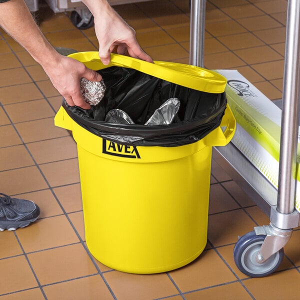 A person holding a yellow trash can with foil in it.
