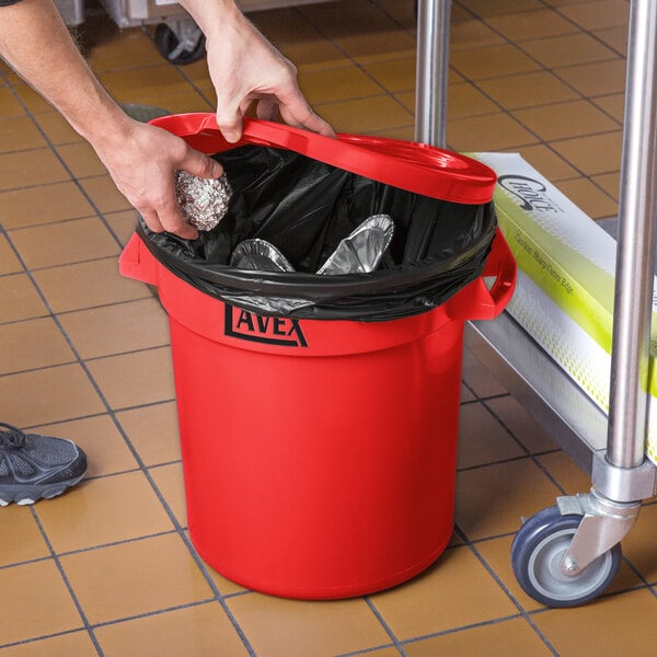 A person's hands putting foil in a red Lavex trash can.