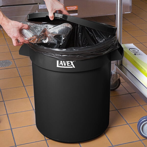 A hand putting foil in a black Lavex commercial trash can.