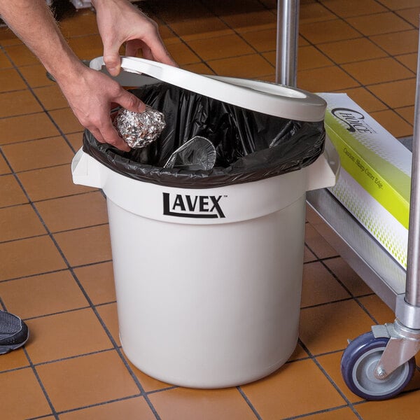 A person opening a Lavex white round trash can with a lid.