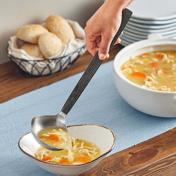 A person using an American Metalcraft stainless steel wavy ladle to pour soup into a bowl.