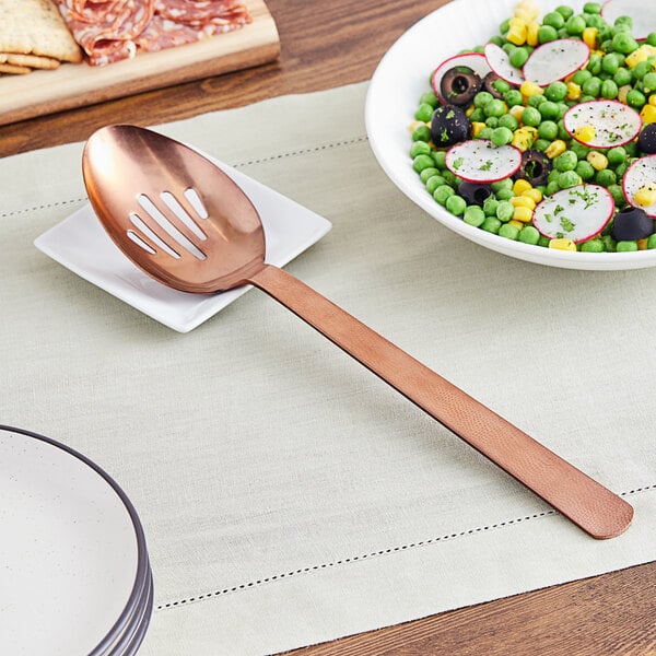 A bronze slotted spoon on a plate of vegetables.