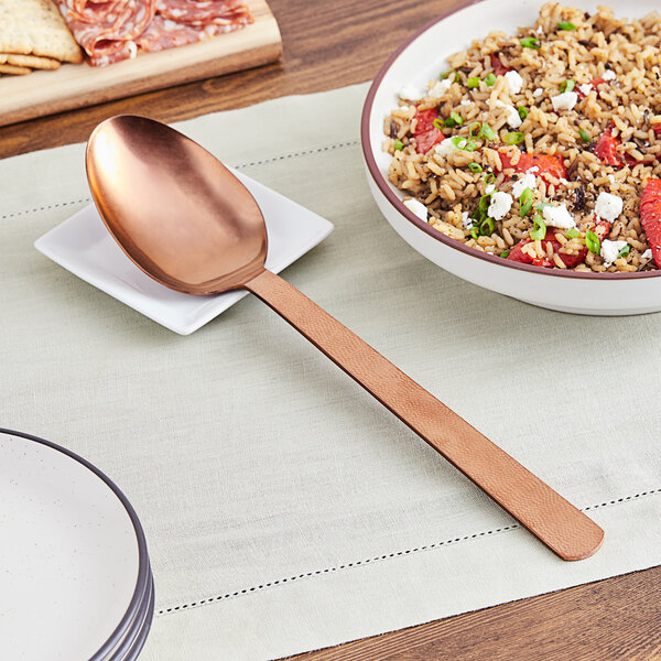 An American Metalcraft hammered bronze solid spoon next to a bowl of rice and vegetables.