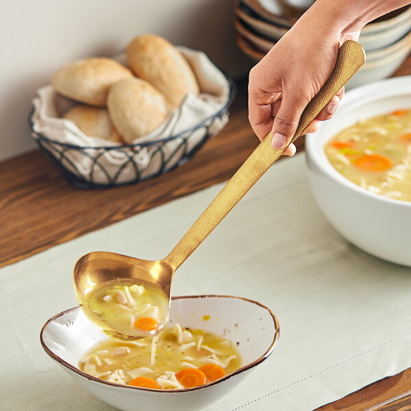 A person using an American Metalcraft hammered gold vintage ladle to serve soup with noodles and carrots.